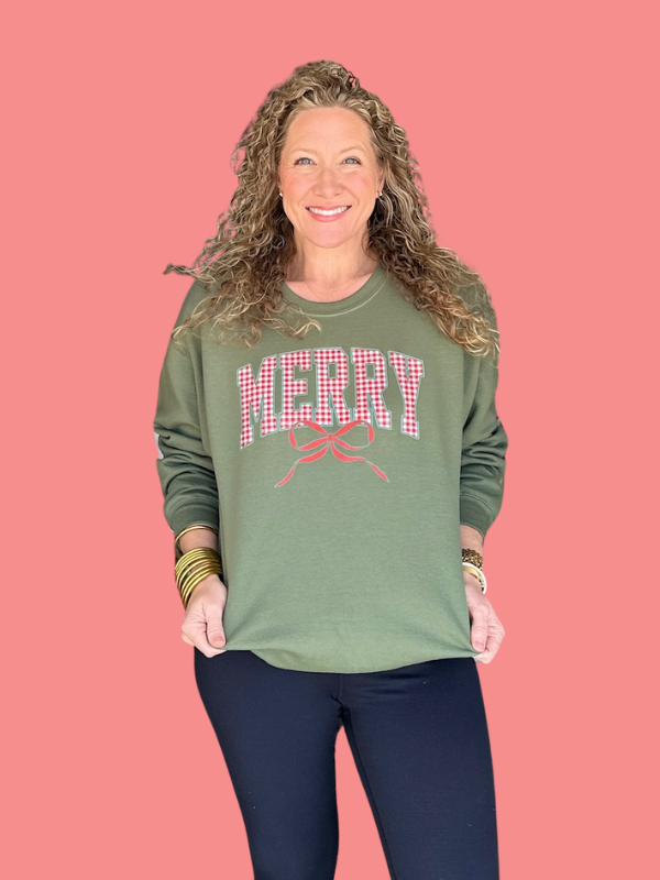 Woman wearing a green sweatshirt with 'MERRY' text on a pink background