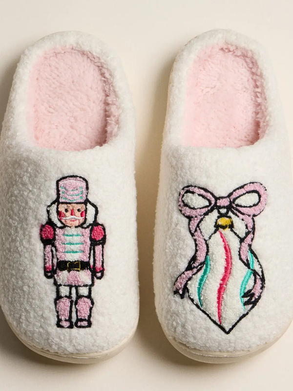 Pair of white slippers with embroidered designs on a beige background