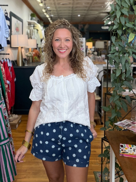 Woman wearing a white top and blue polka dot shorts in a store setting