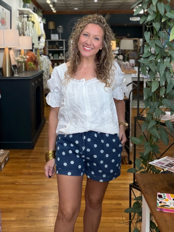 Woman in a white blouse and navy polka dot shorts standing in a store.