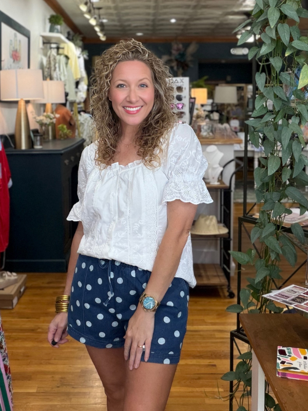 Woman in a white blouse and blue polka dot shorts standing in a store.