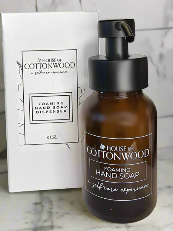Brown foaming hand soap dispenser with black pump and 'House of Cottonwood' branding on a marble surface.