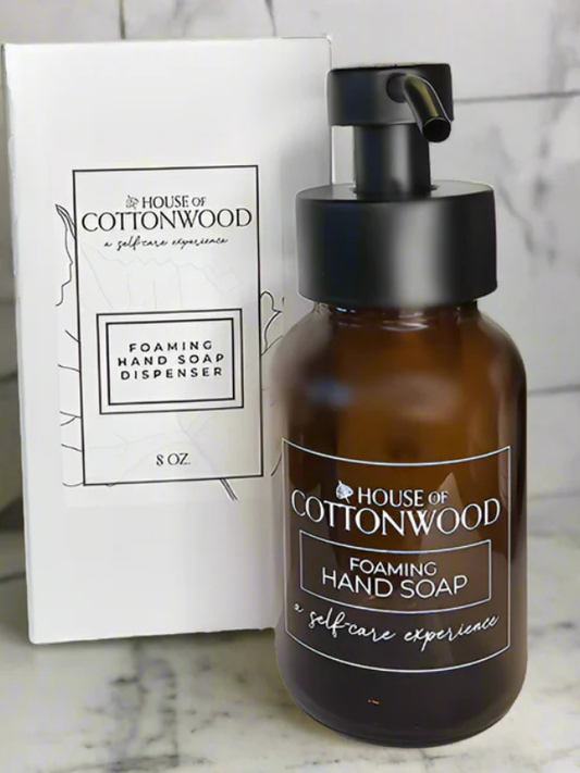 Brown foaming hand soap dispenser with black pump and 'House of Cottonwood' branding on a marble surface.
