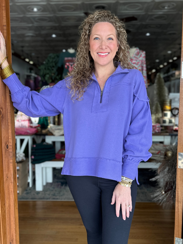 Woman wearing a purple sweatshirt standing in a doorway with a store interior in the background.