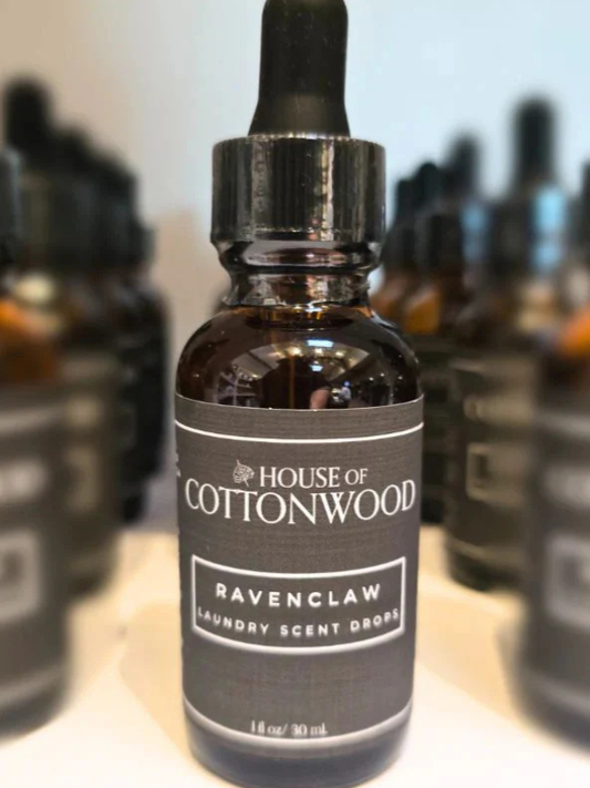 Bottle of House of Cottonwood Ravenclaw laundry scent drops with a blurred background of similar bottles.