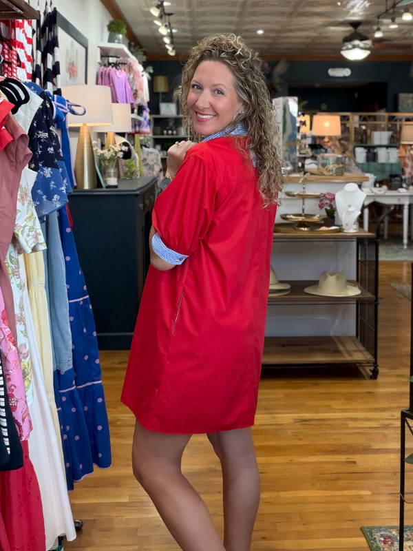 Woman in a red dress standing in a store with clothing racks and displays.