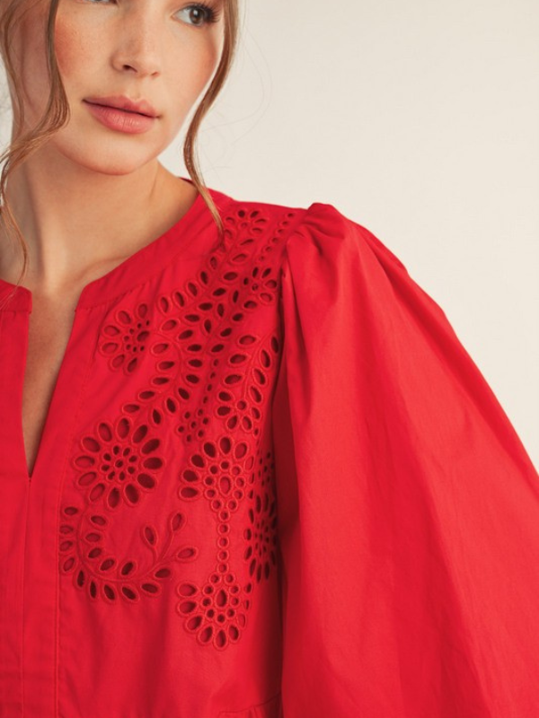 Red blouse with intricate black lace detailing on a plain background