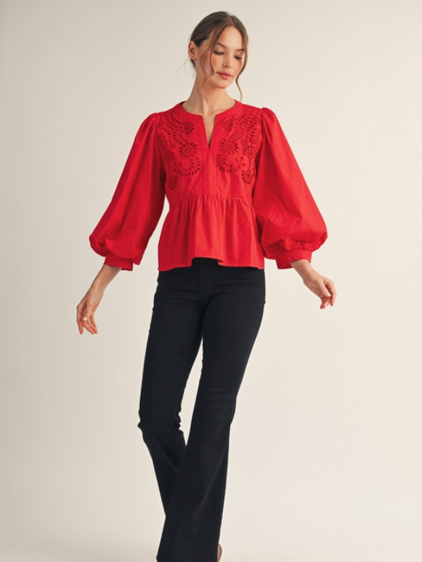 Woman wearing a red blouse with black pants on a plain background
