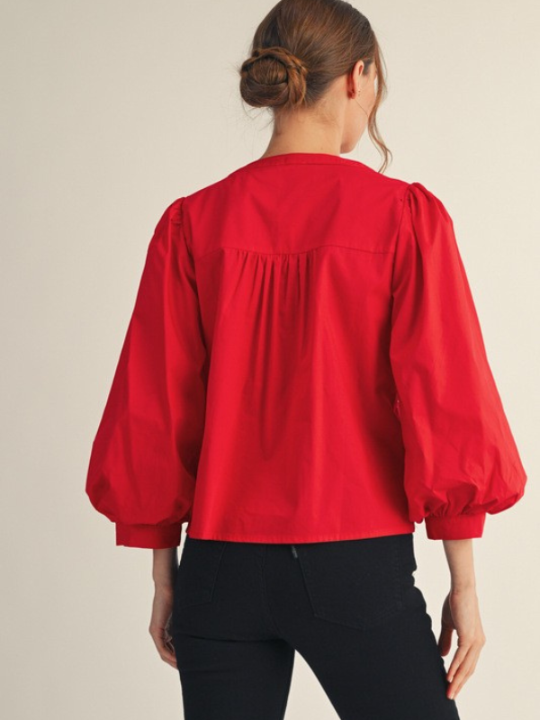 Red blouse with puffed sleeves worn by a person on a beige background