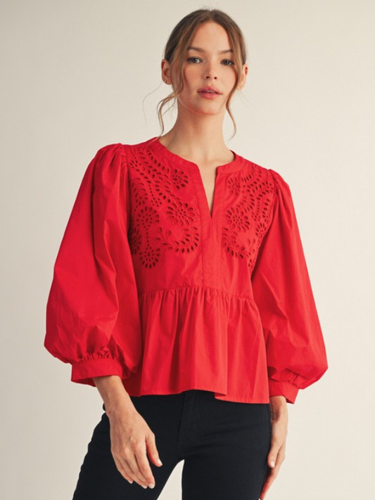 Woman wearing a red blouse with intricate cut-out design on a plain background