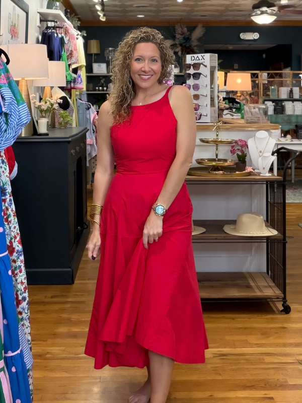 Woman in a red dress standing in a store with various items on shelves and tables.