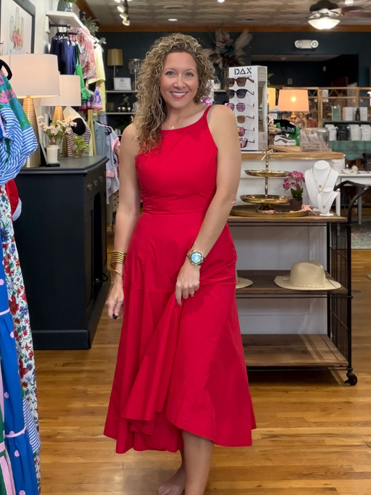 Woman in a red dress standing in a store with various items on shelves and tables.