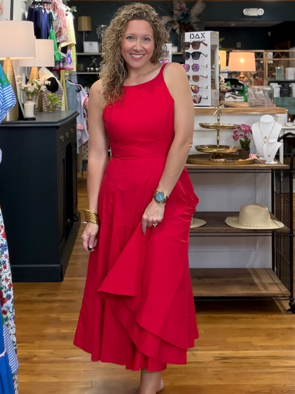 Woman in a red dress standing in a store with various items on shelves in the background.