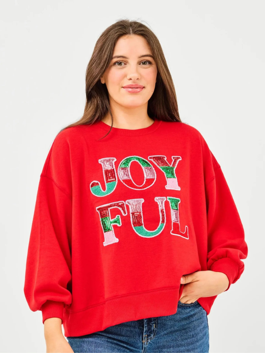 Woman wearing a red sweatshirt with 'JOYFUL' printed on it against a plain background