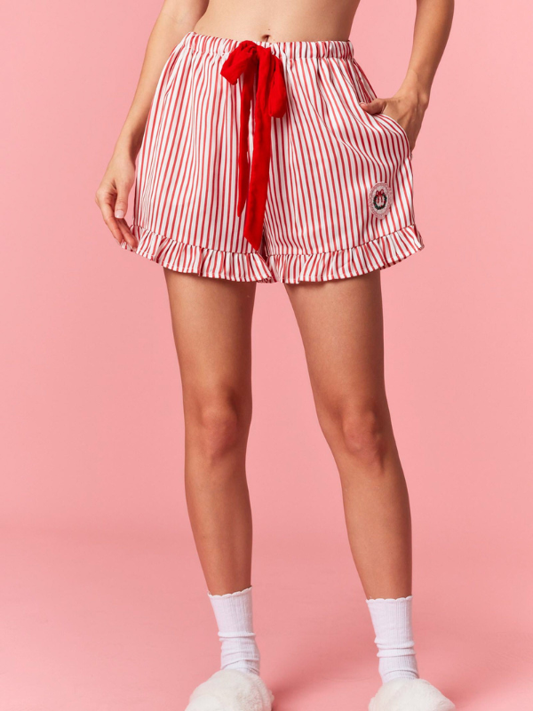 Person wearing red and white striped shorts with a red bow on a pink background