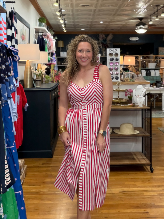Woman in a red and white striped dress standing in a store with clothing racks and displays.