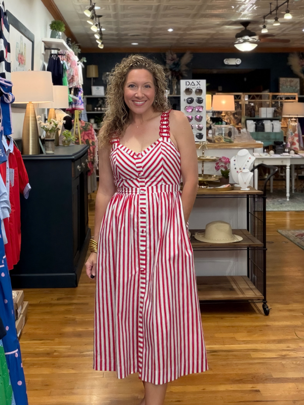 Woman in a red and white striped dress standing in a store with various items on shelves and tables.