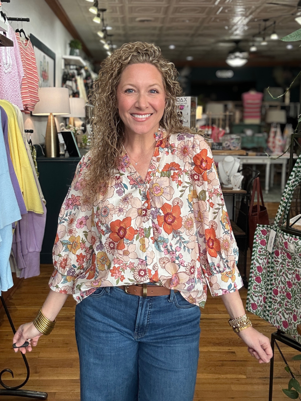Woman wearing a floral blouse and jeans in a store setting