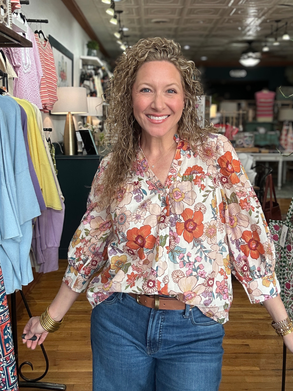 Woman wearing a floral blouse and jeans in a store setting