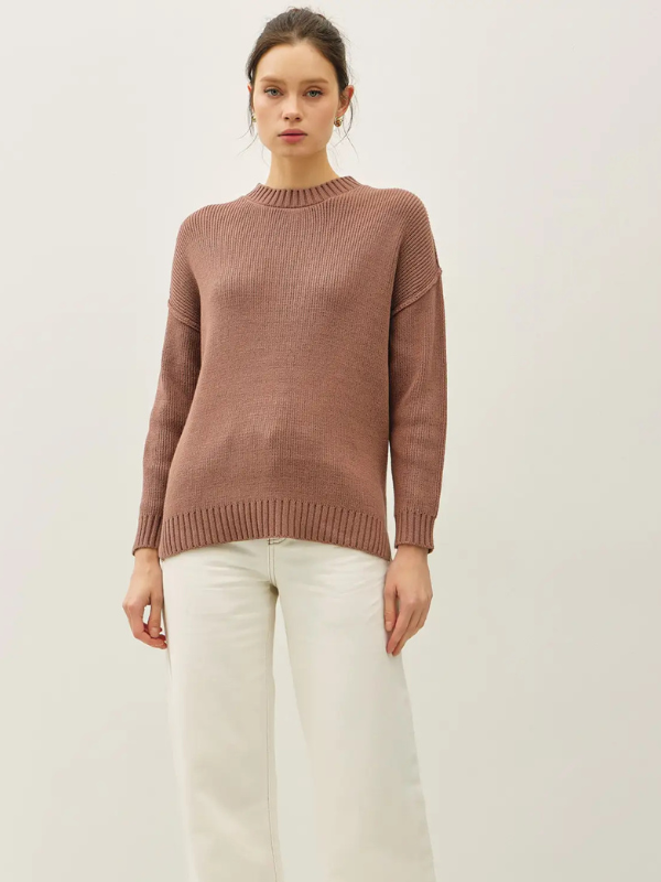 Woman wearing a brown sweater and white pants on a light background