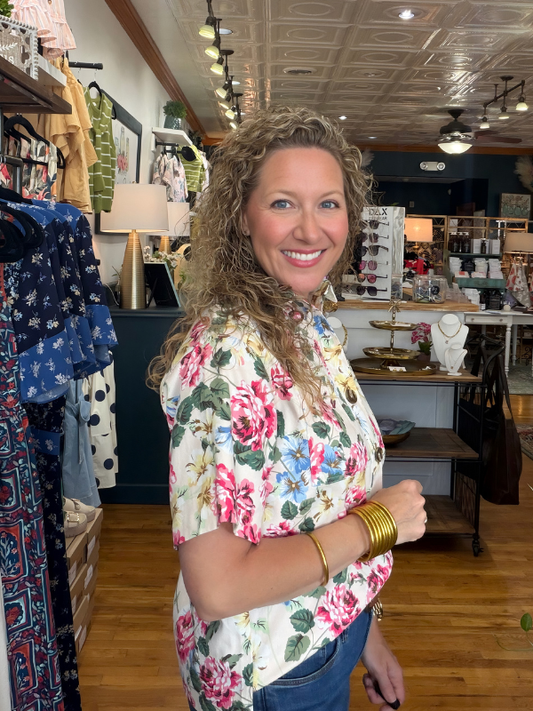Woman in a floral shirt standing in a store with clothing racks and displays.