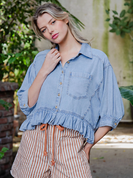 Woman wearing a denim shirt with ruffled bottom and striped pants outdoors.