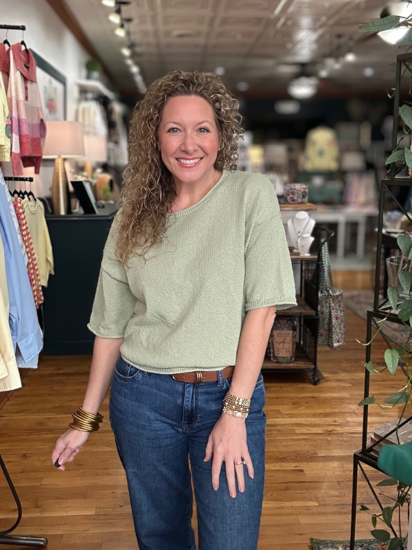 Woman wearing a green top and blue jeans in a store setting