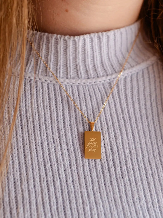 Gold necklace with a rectangular pendant on a light gray sweater