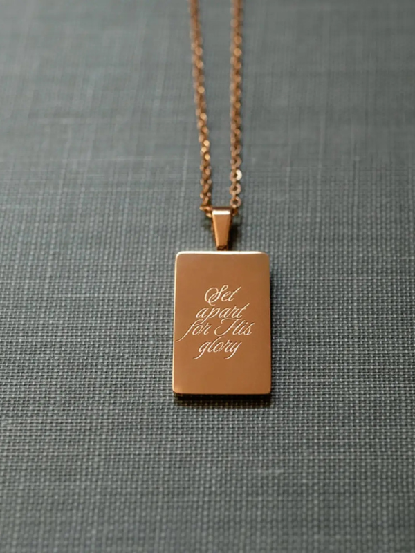 Rose gold necklace with a rectangular pendant on a gray fabric background
