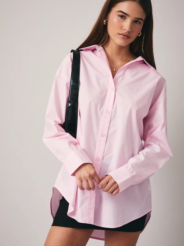 Woman wearing a pink long-sleeve shirt over a black swimsuit against a plain background