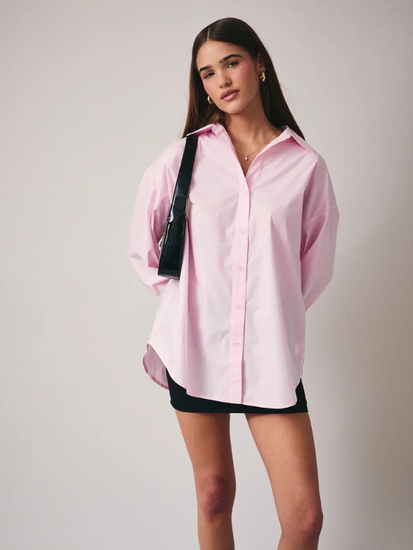 Woman wearing a pink shirt and black shorts against a plain background