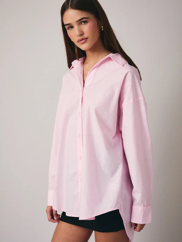 Woman wearing a pink oversized shirt and black shorts on a plain background