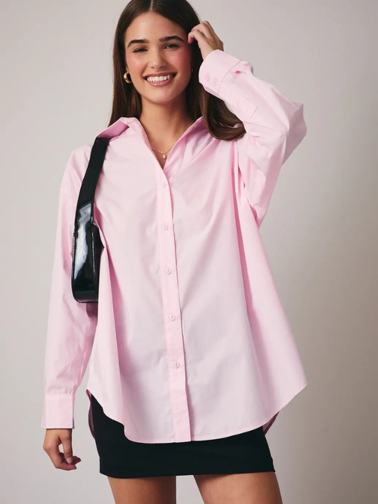 Woman wearing a pink shirt and black skirt with a black bag on a plain background