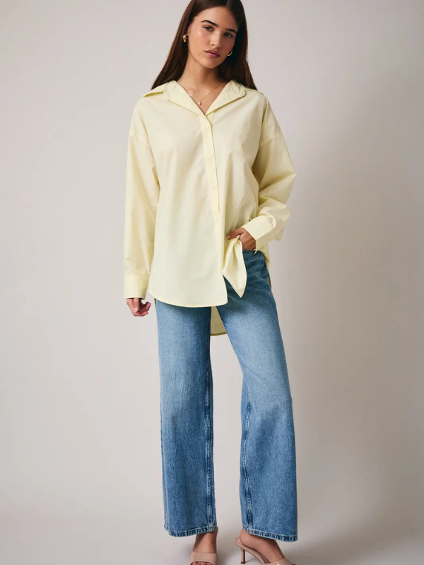 Woman wearing a light yellow blouse and blue jeans against a plain background