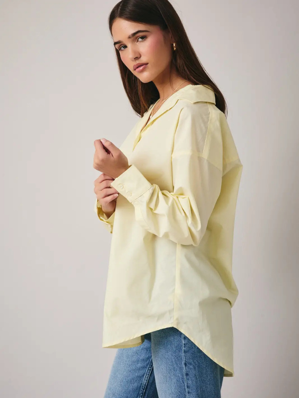 Woman wearing a light yellow blouse and blue jeans against a plain background