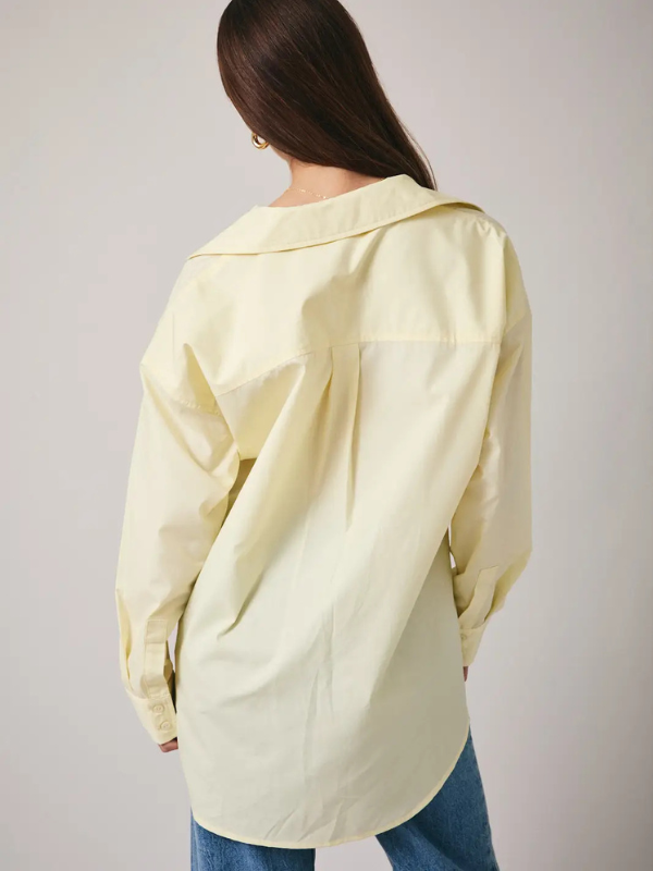 Person wearing a light yellow oversized shirt with a plain background