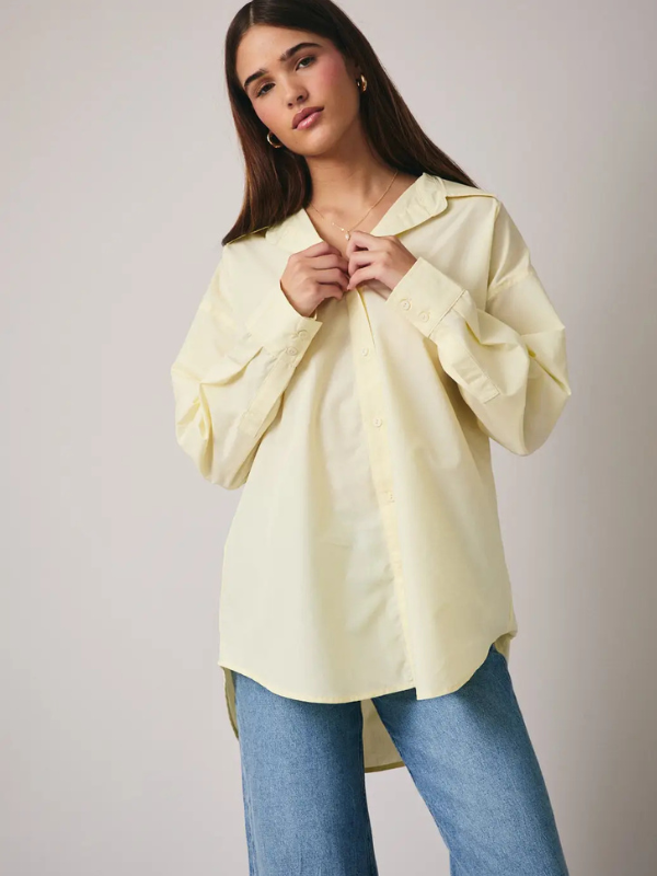 Woman wearing a light yellow blouse and blue jeans against a plain background