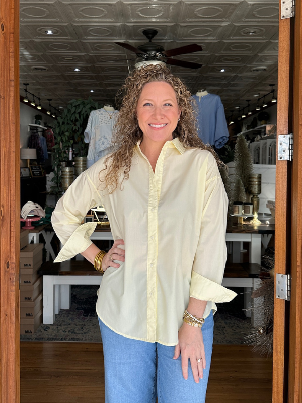 Woman wearing a light-colored blouse and blue jeans standing inside a store.