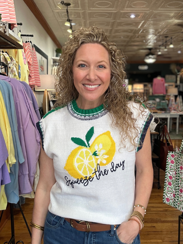Woman wearing a sweater with lemon design and text in a clothing store.