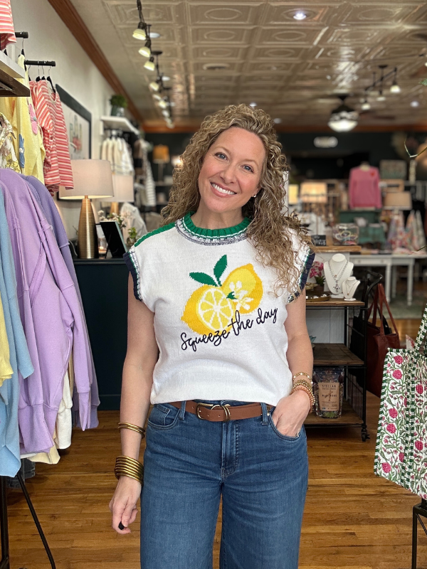Woman wearing a white t-shirt with a lemon graphic and text, standing in a store.