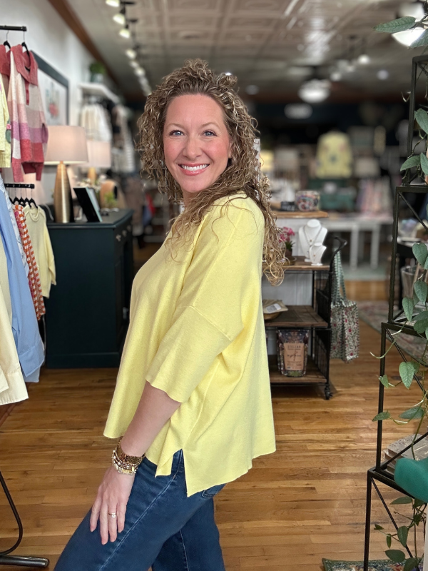 Woman in a yellow top standing in a store with wooden floors and clothing racks.