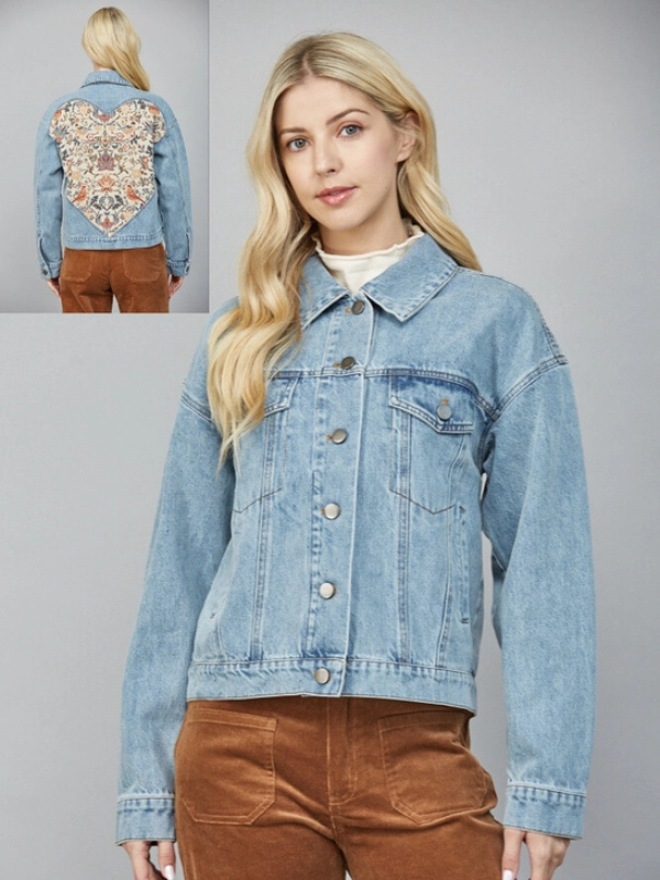 Woman wearing a light blue denim jacket with a detailed back design, standing against a gray background.