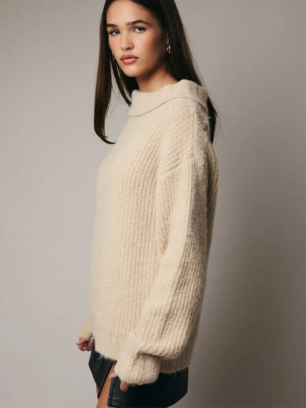 Woman wearing a cream knitted sweater against a plain background