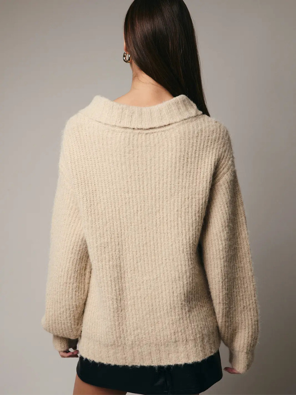 Beige knitted sweater worn by a person on a plain background