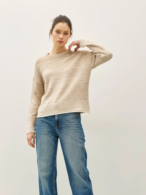 Woman wearing a beige sweater and blue jeans against a plain background