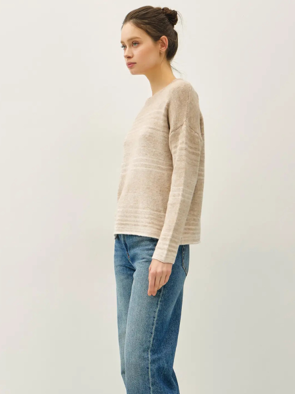 Woman wearing a beige sweater and blue jeans on a plain background