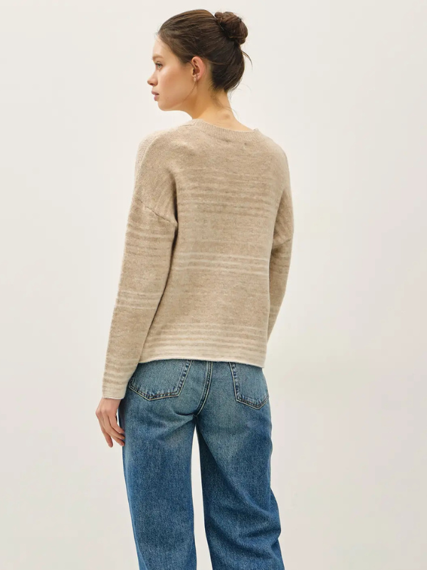 Person wearing a beige sweater and blue jeans against a plain background