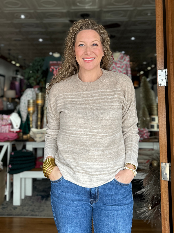 Woman wearing a beige sweater and blue jeans standing in a store.