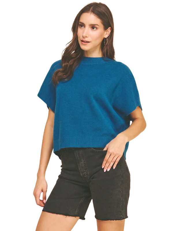 A woman modeling a teal blue short-sleeve knit sweater with black denim shorts against a plain white background.