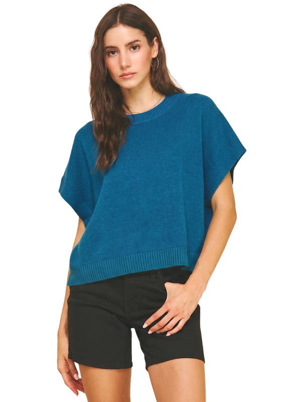 A woman modeling a teal blue short-sleeve knit top with black shorts against a plain white background.